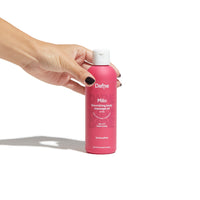 Olio massaggi Milo Dafne, alla vaniglia, naturale, in flacone magenta impugnato da una mano, su sfondo bianco