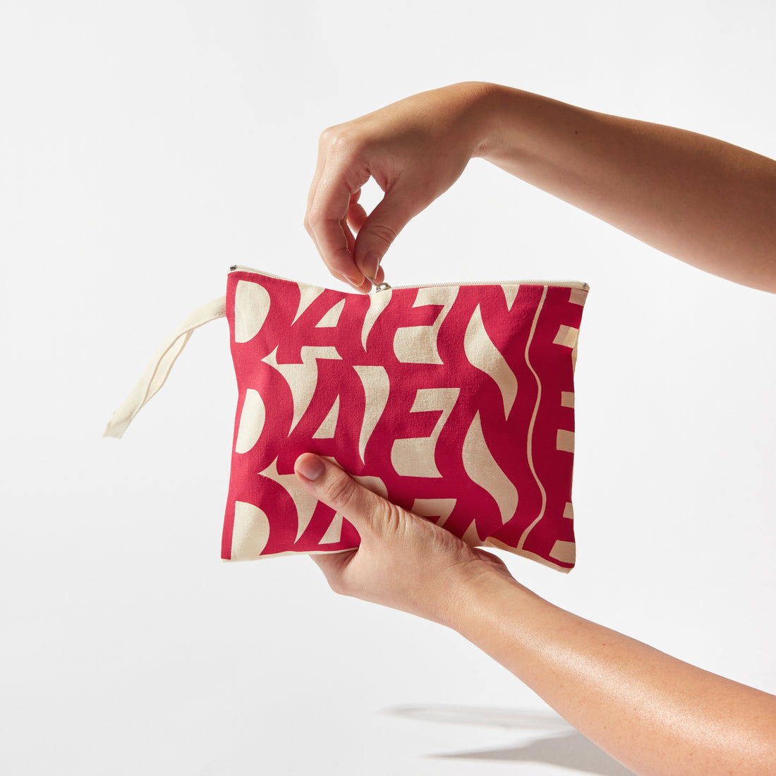 Pochette Dafne in tessuto con stampa rossa su fondo naturale, tenuta in mano, sfondo bianco